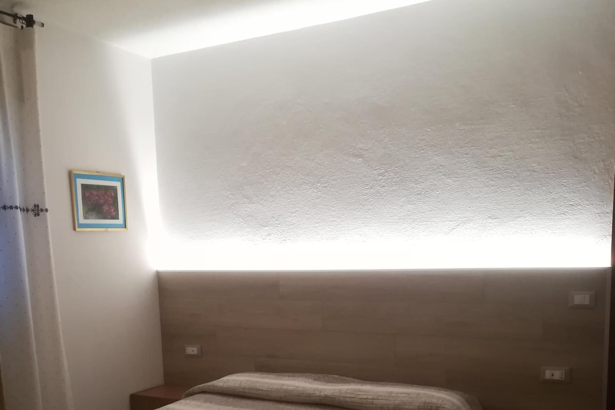 A bedroom with a bed, two nightstands, a wall-mounted light, and a framed picture.