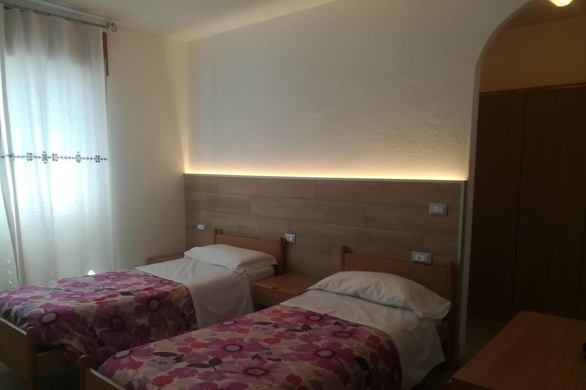 A room with two single beds, each with a floral bedspread, wooden headboards, and bedside tables.