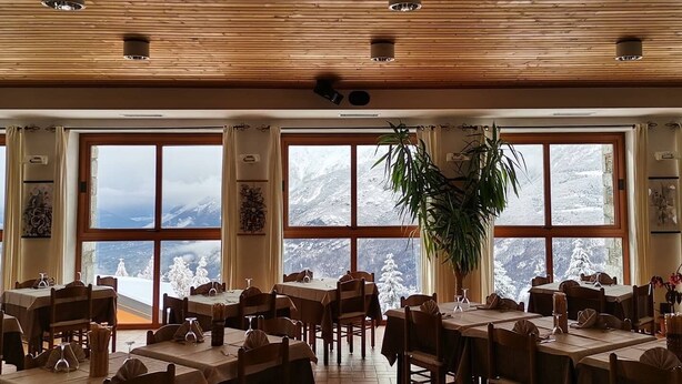 A restaurant with wooden ceiling and large windows offering mountain views. Tables are set with chairs and have wine glasses and napkins. - Albergo Sargas (Cevo)