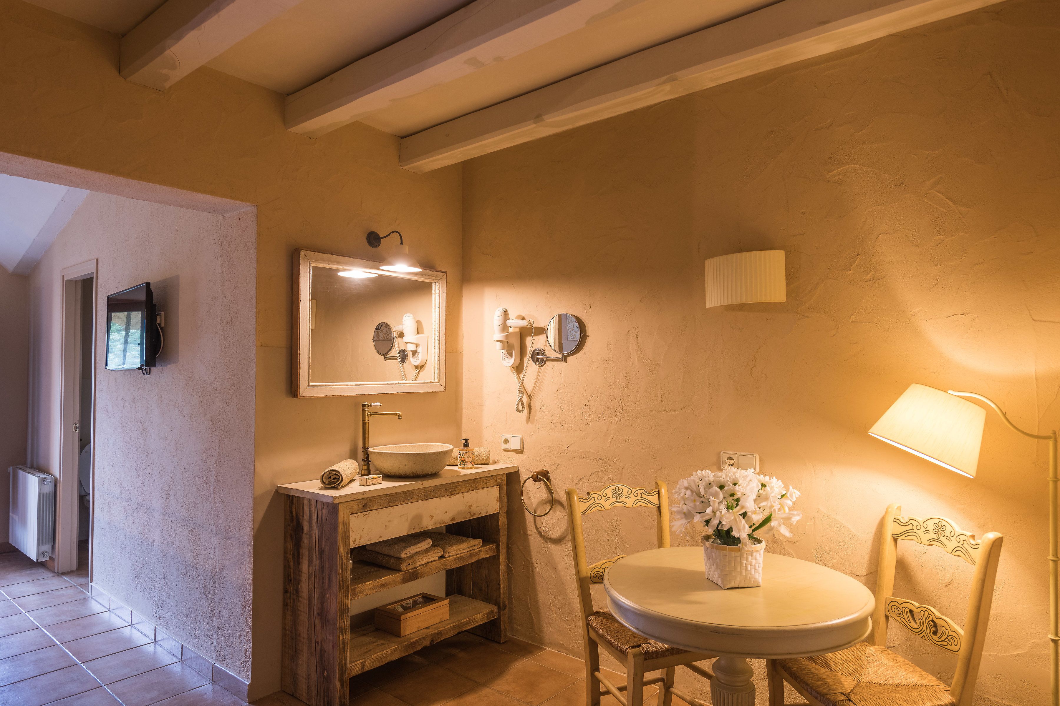Un baño con tocador de madera, un espejo redondo, un lavabo y una silla con un florero.