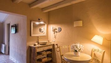 Un baño con tocador de madera, un espejo redondo, un lavabo y una silla con un florero.