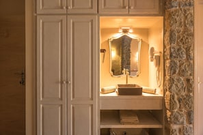 Une salle de bain avec un meuble-lavabo, un miroir, une serviette et un mur en pierre.