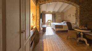Een slaapkamer met een stenen boog, een bed, een tafeltje en een rieten stoel.