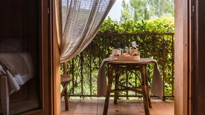 Een balkon met een ontbijttafel, een rieten stoel en uitzicht op groen.
