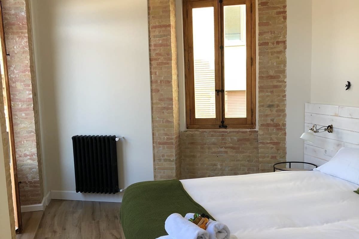 A hotel room with a large bed, a radiator, a window with blinds, and a brick wall.