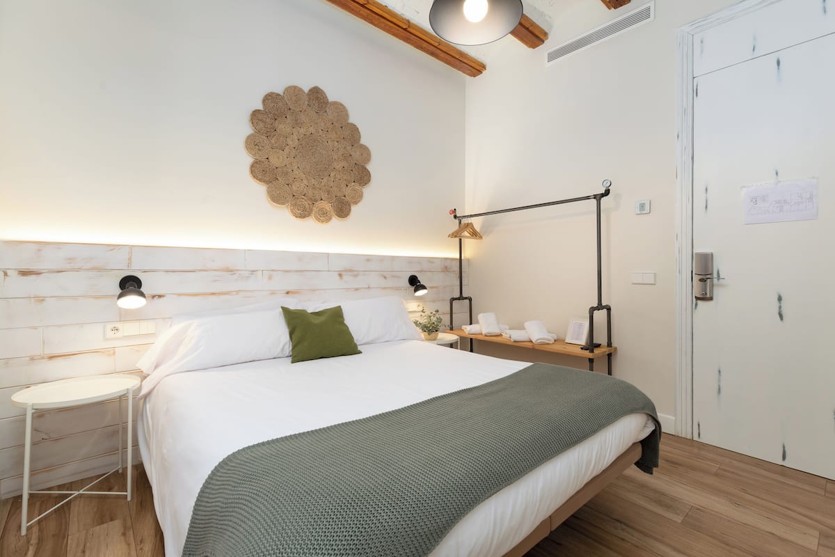A neatly arranged bedroom with a bed, bedside tables, a wall-mounted light fixture, and a door with a sign.