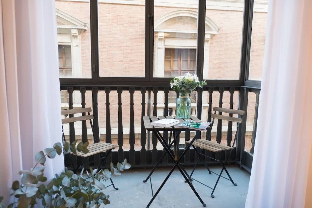 A balcony with two wooden chairs, a small table, and a vase with flowers.