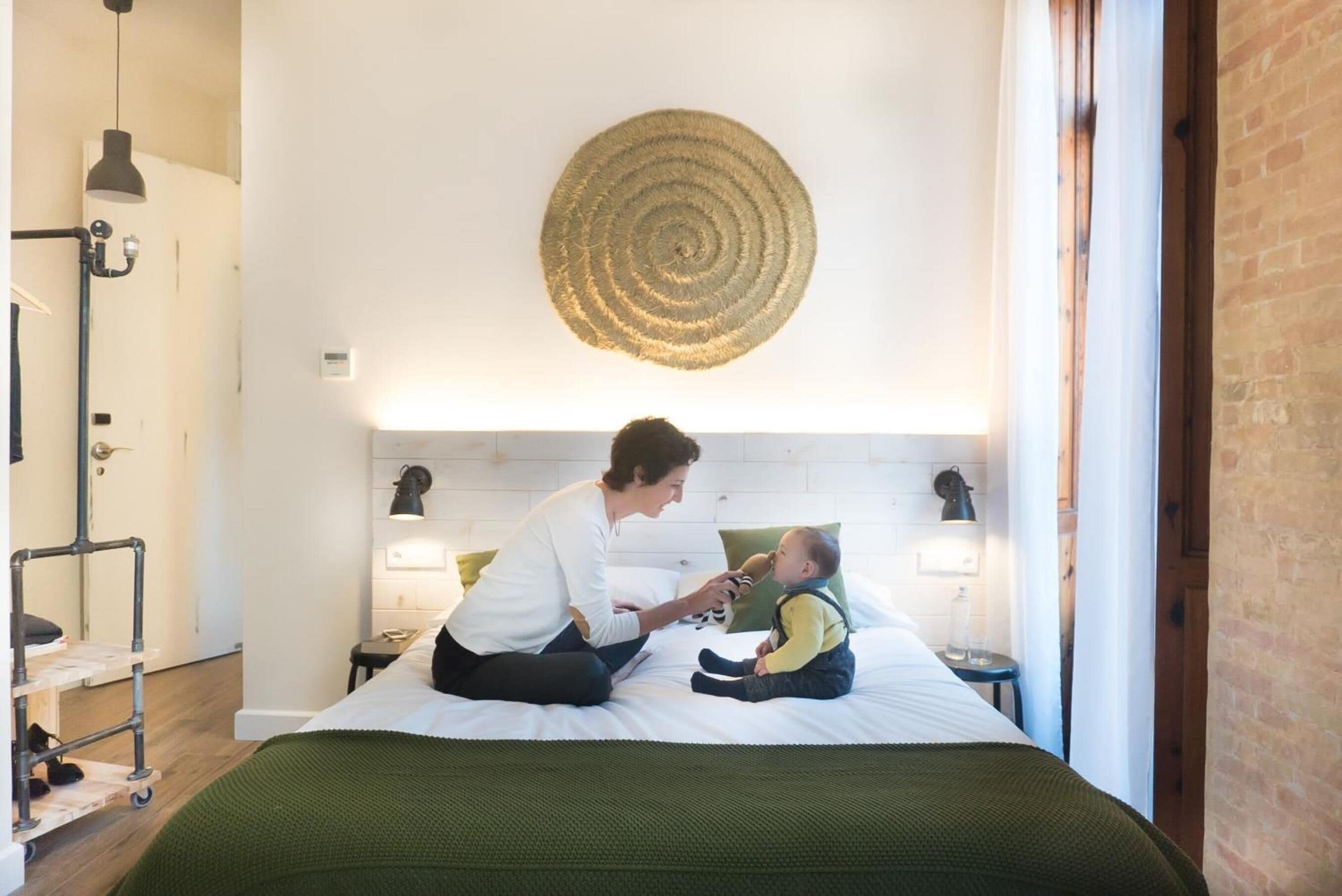 A room with a bed, a circular wall hanging, and a small table with a lamp.