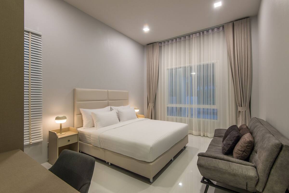 A modern bedroom with a large bed, bedside tables, a desk, and a sofa.