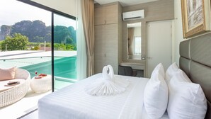 A hotel room with a large bed, a sitting area with a view of the mountains, and a balcony with a pool. - The Haven Krabi (Krabi)