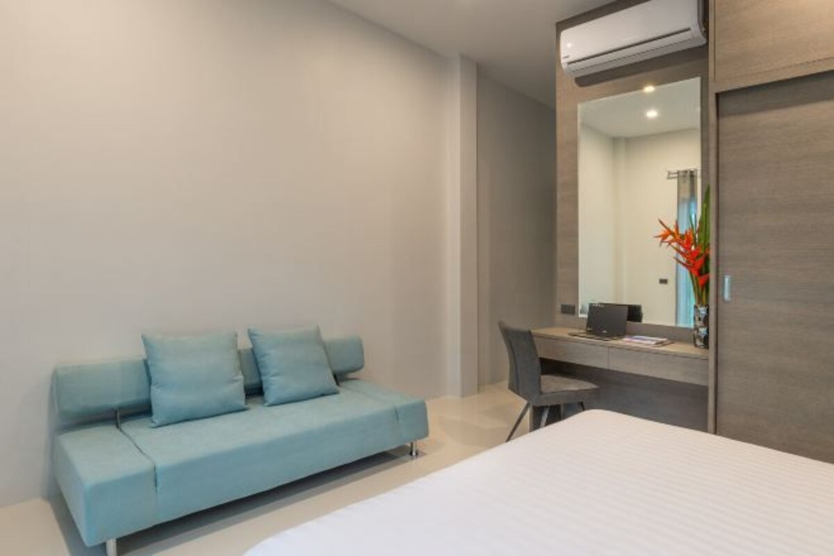 Habitación de hotel moderna con cama, sofá azul claro, escritorio con silla y un espejo grande.