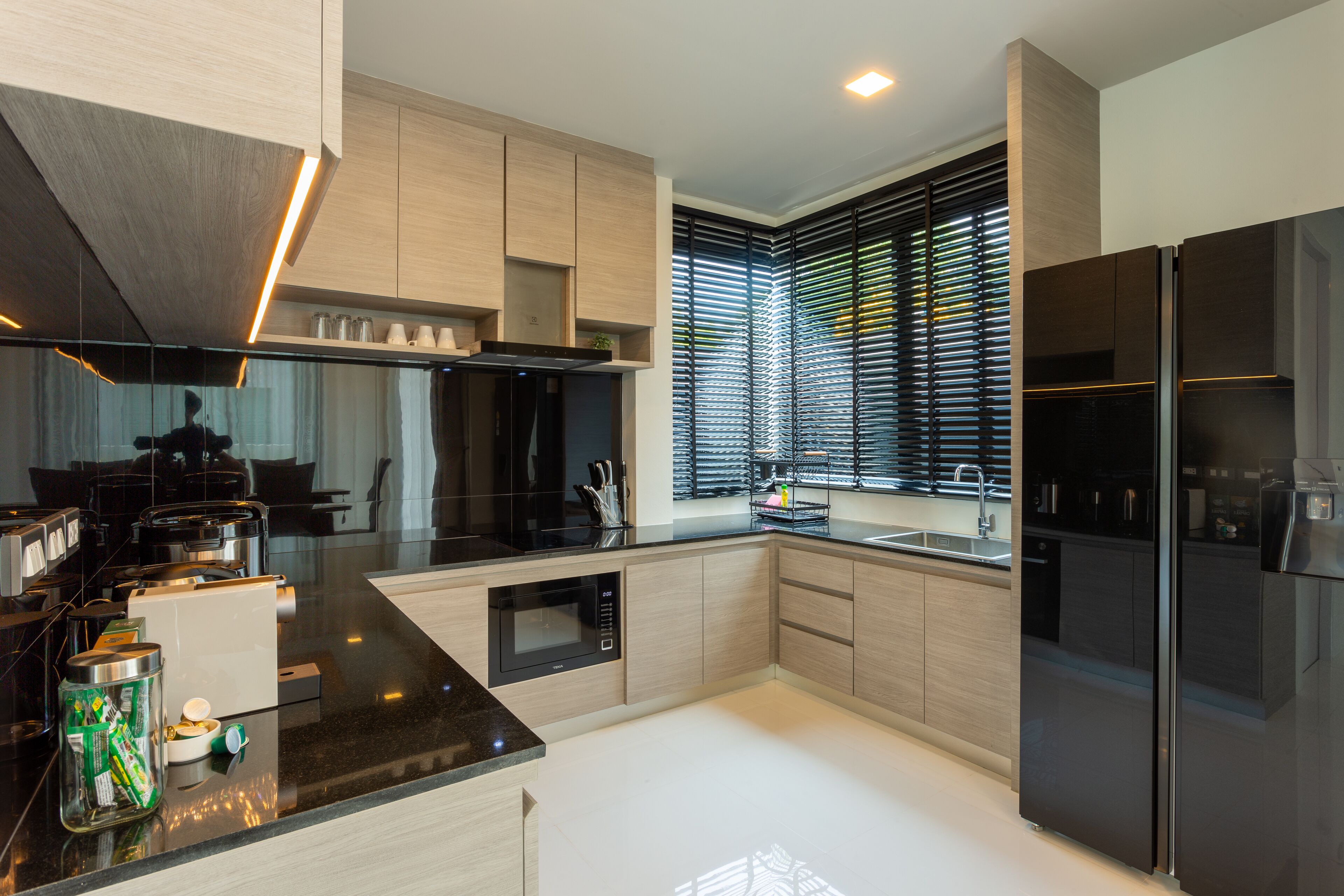 A modern kitchen with black appliances, wooden cabinets, and a large window with blinds.