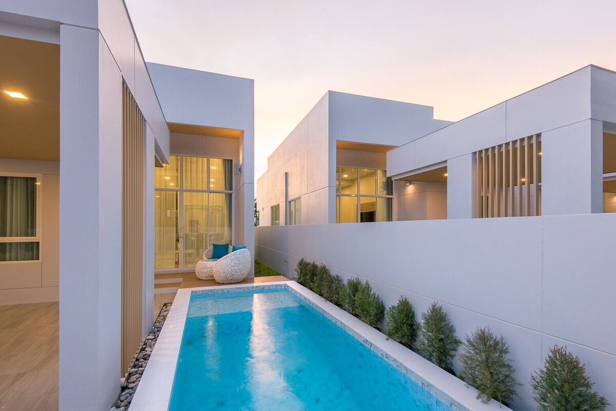 A modern house with a swimming pool, white walls, and a glass door leading to a patio area with outdoor seating.
