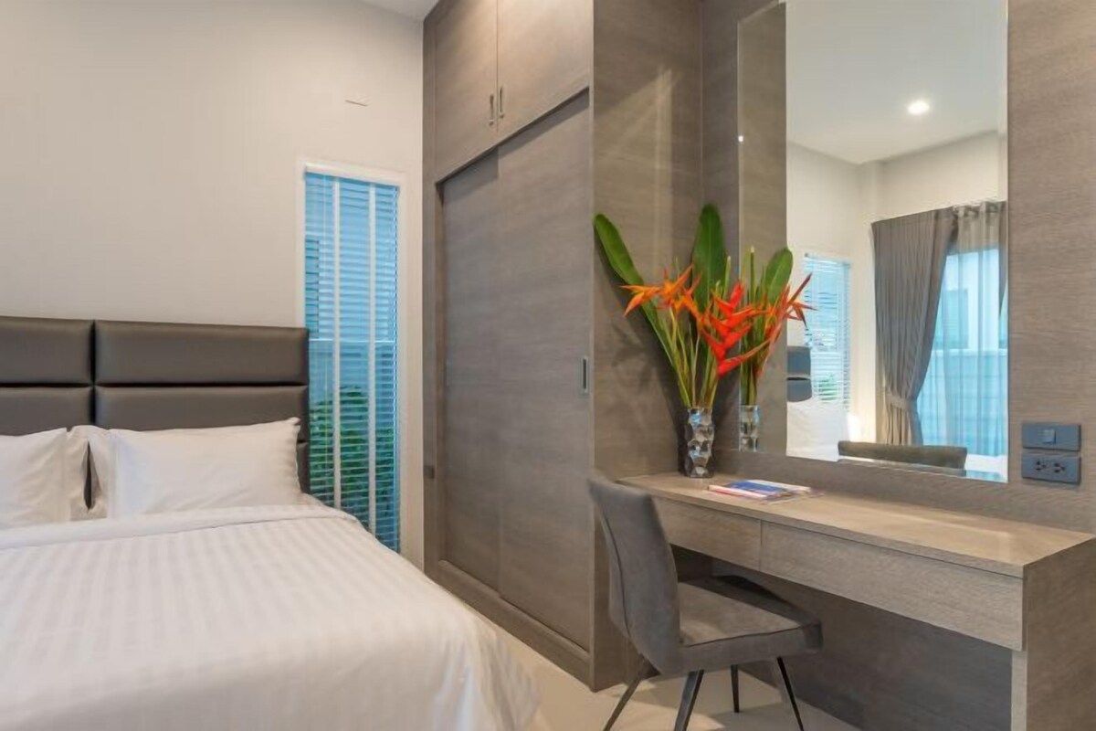 A hotel room with a bed, a desk, a chair, a mirror, and a window with blinds.