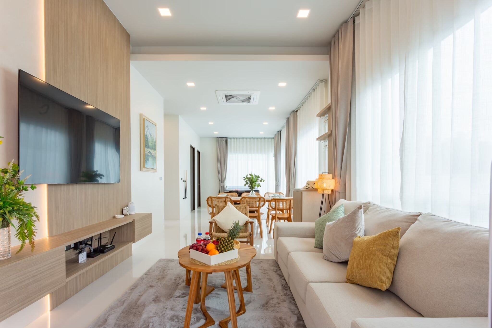 Una sala de estar moderna con un televisor de pantalla plana, una zona de comedor con mesa y sillas, y un sofá con cojines.