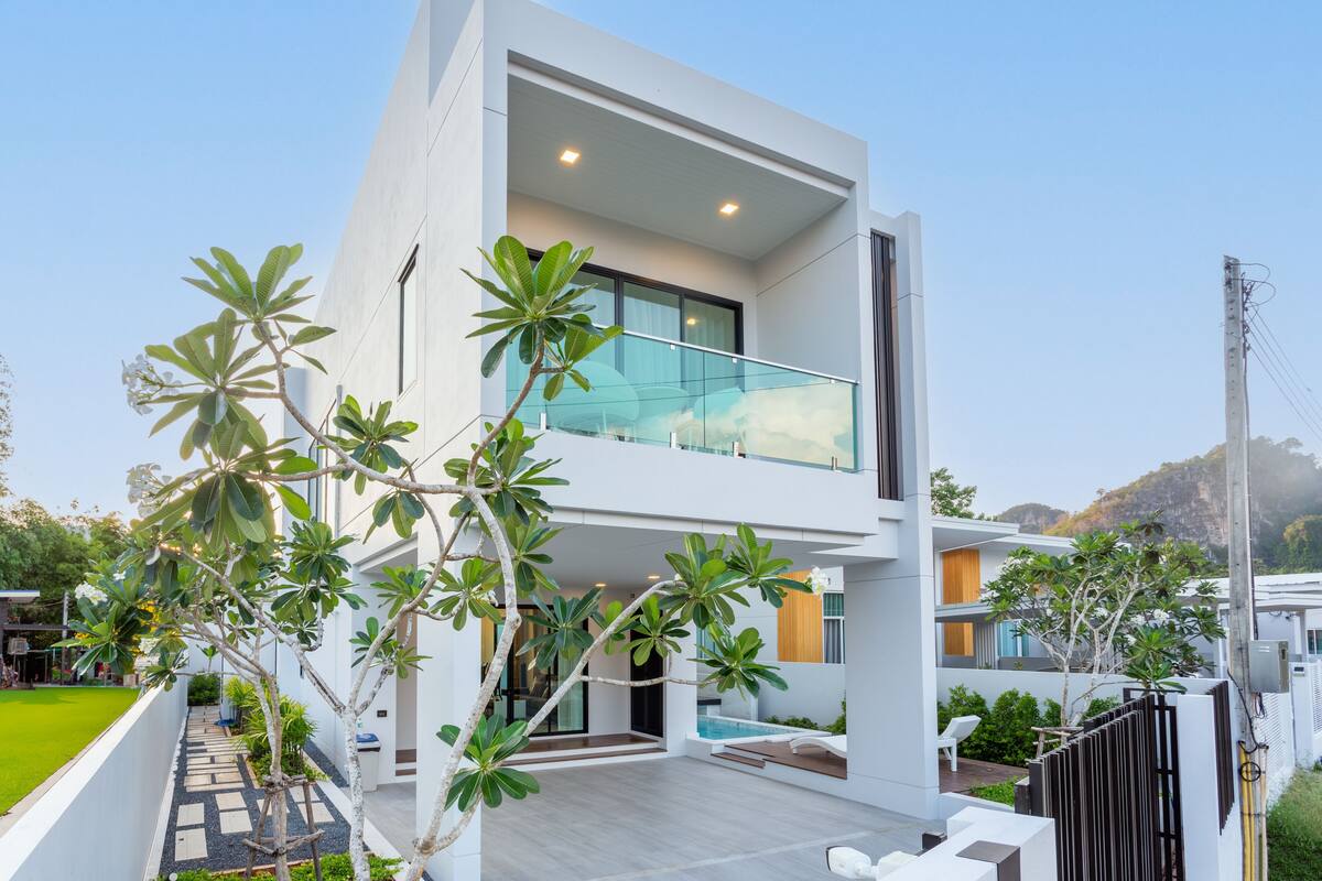 A modern two-story house with a balcony, a swimming pool, and a well-maintained garden.