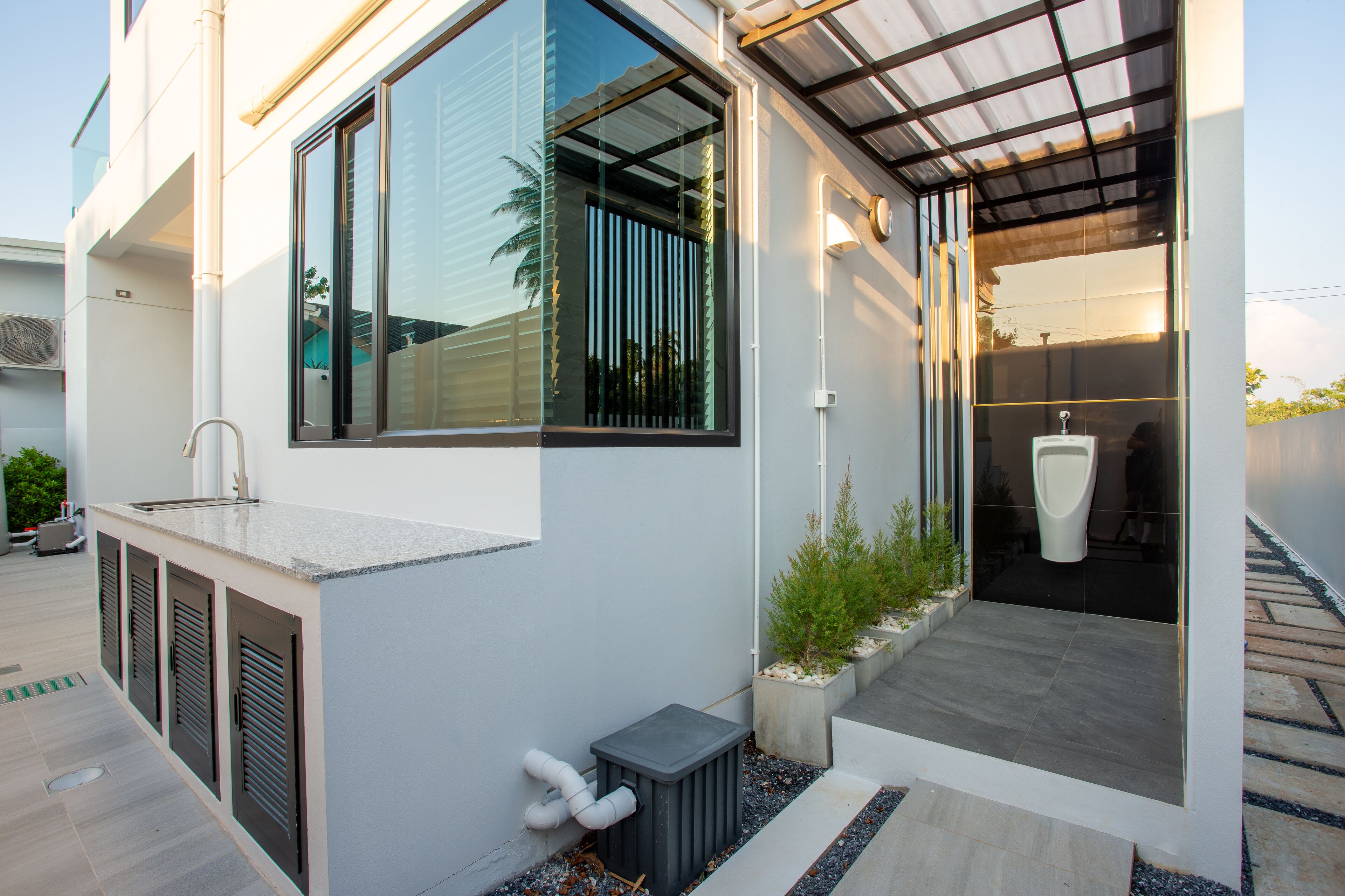 A modern building with a large window, a covered outdoor area, and a visible urinal.