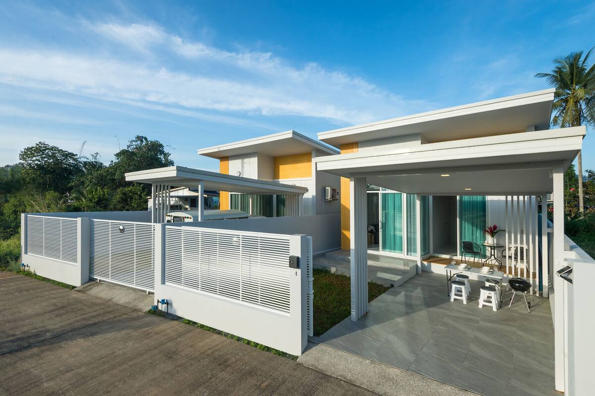 A modern house with a covered patio, a fenced yard, and a clear sky.