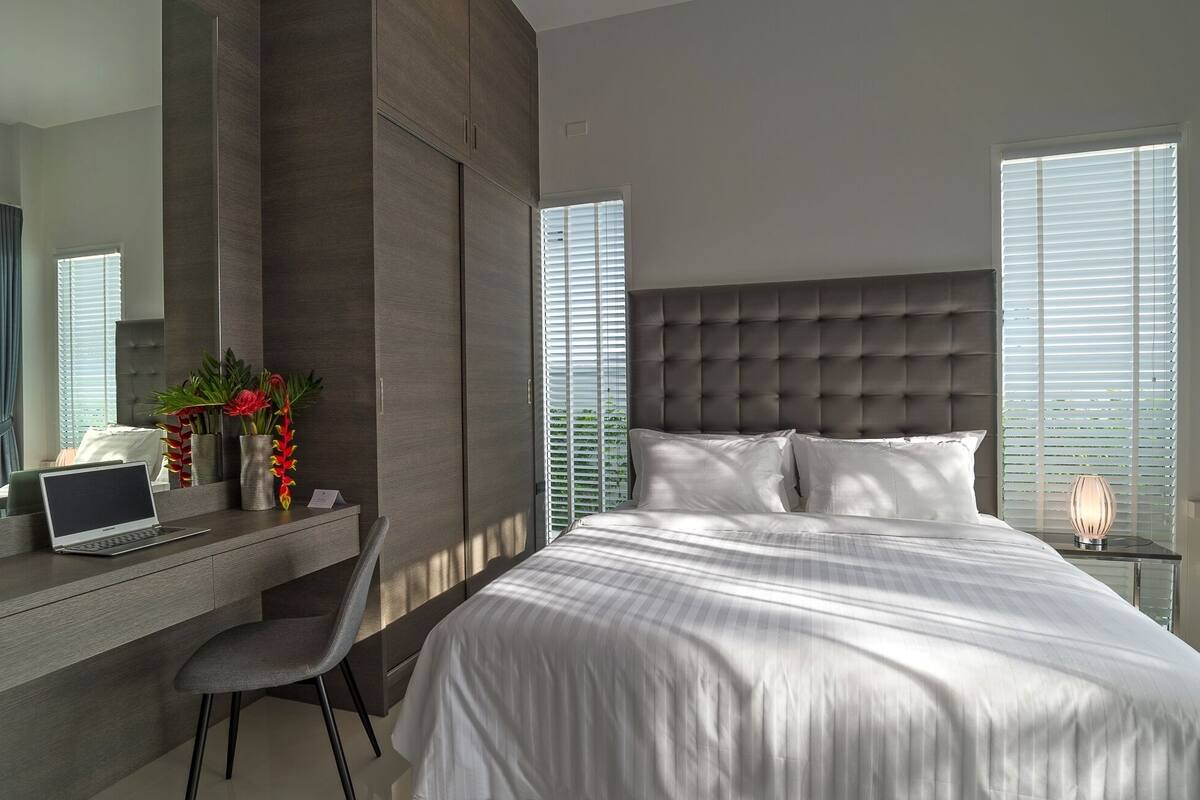 A modern bedroom with a large bed, a desk with a laptop, and a chair.