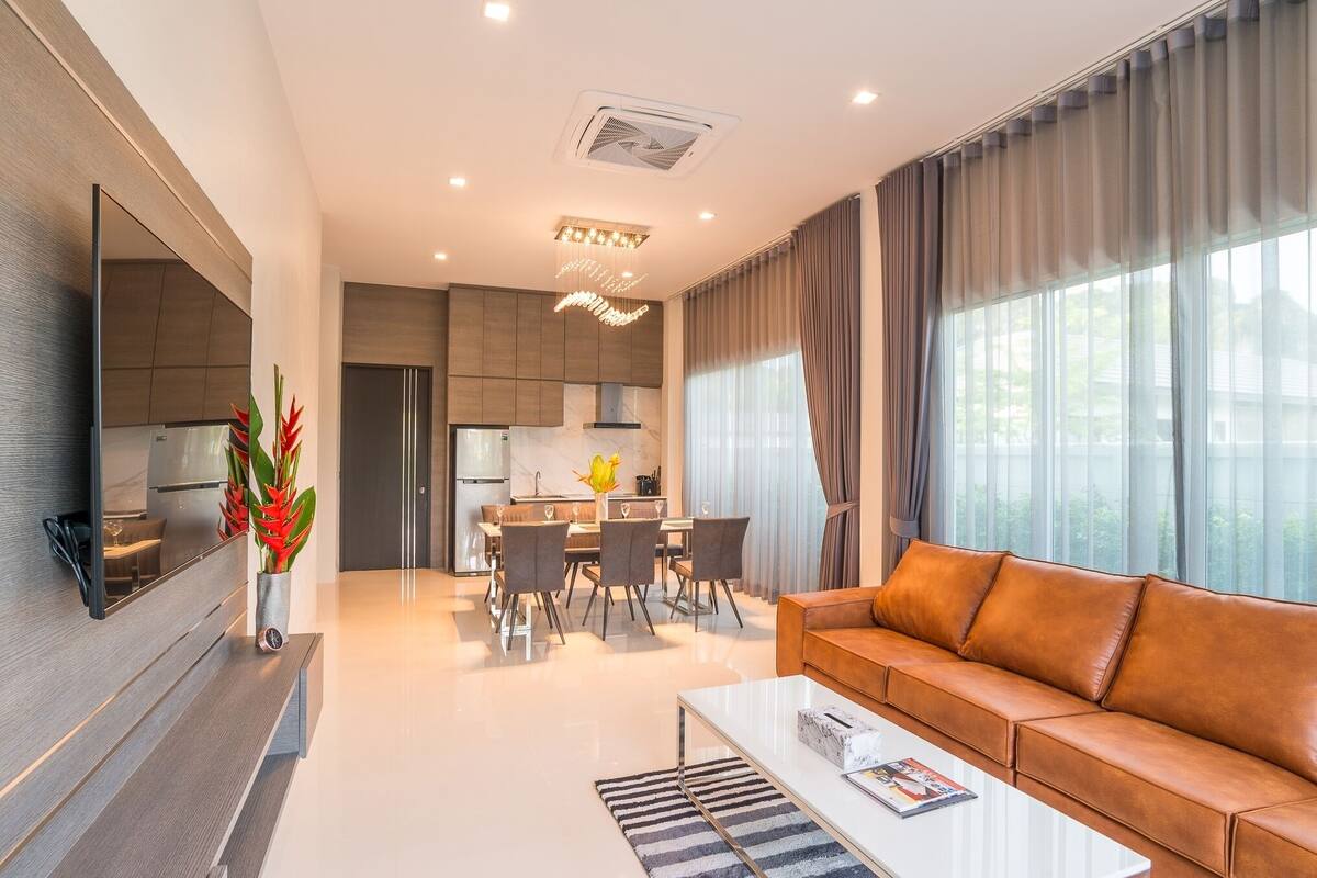 A modern living room with a sofa, coffee table, and a dining area with chairs and a kitchen in the background.