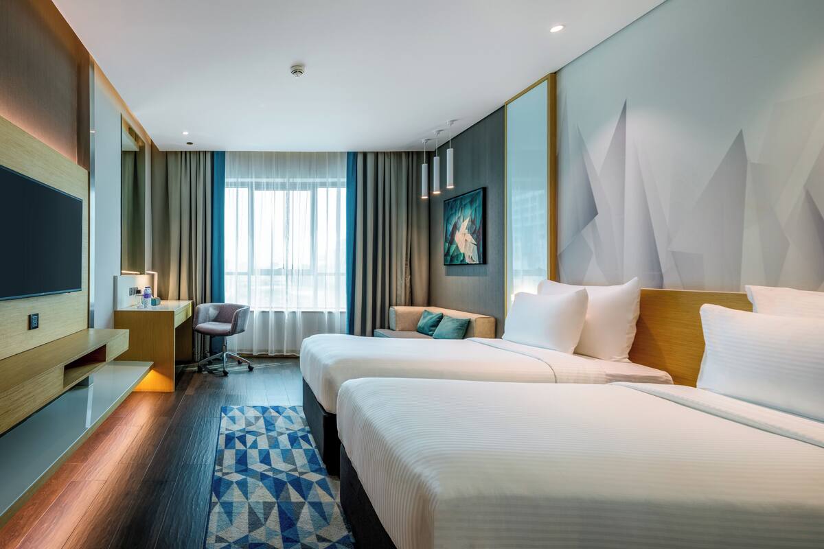 Une chambre d’hôtel avec deux lits, un bureau, une chaise, une télévision et une grande fenêtre avec des rideaux.