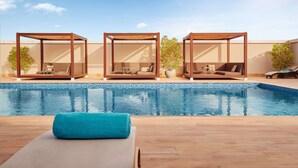 Un espace aménagé au bord de la piscine, comprenant trois petits pavillons en bois, chacun doté d’un coin salon avec des coussins et d’une petite table.