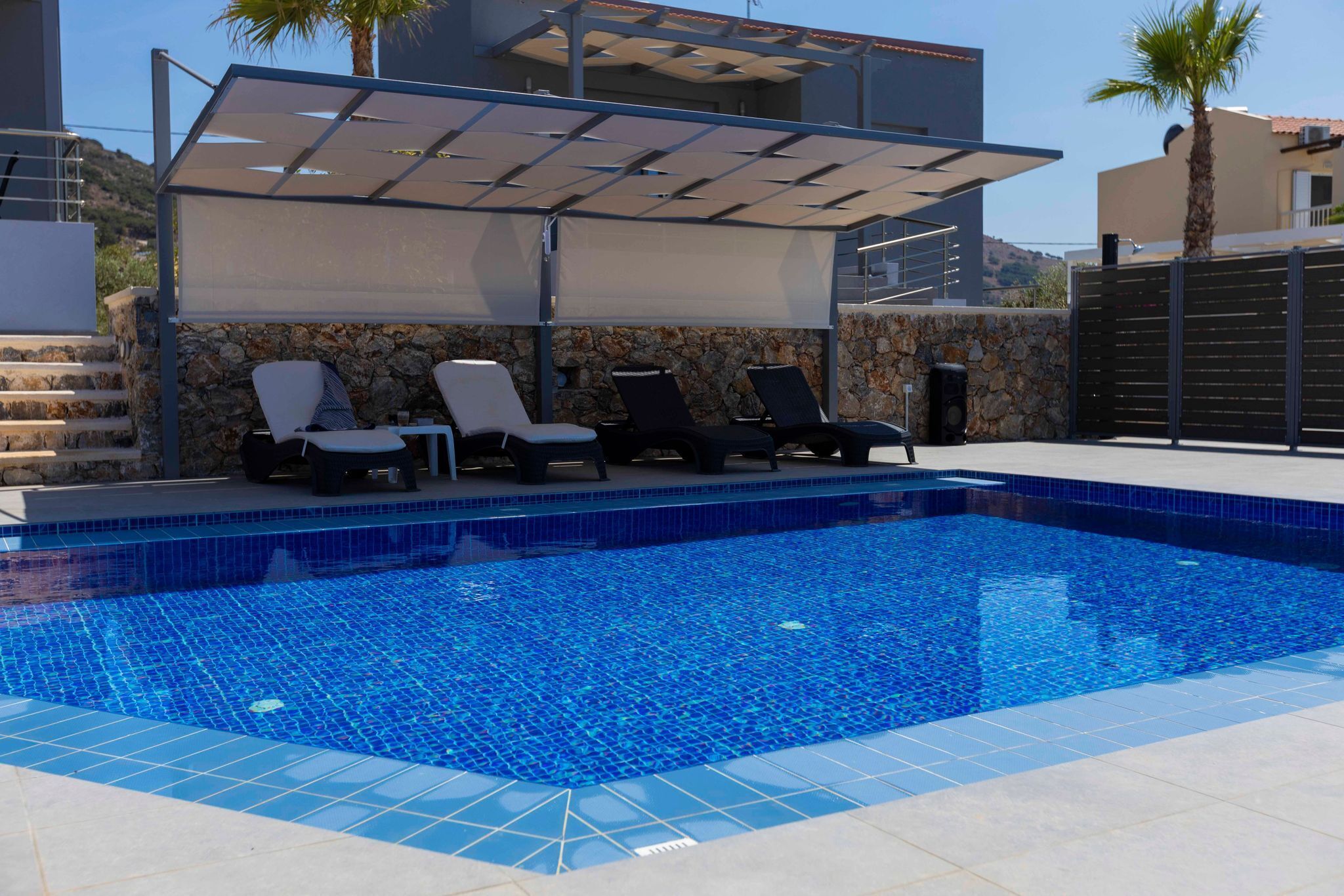 A swimming pool with tiled blue edges, surrounded by lounge chairs and a covered seating area.