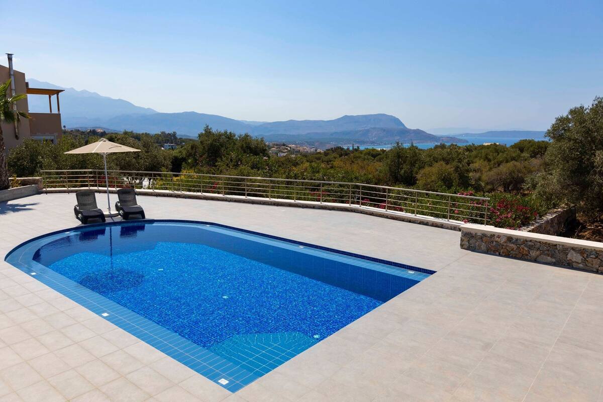 Una piscina con vistas a las montañas, un área de estar cubierta y un muro de contención de piedra.