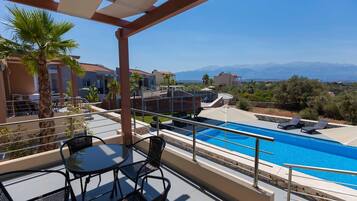 Zona de piscina en la azotea con vistas despejadas a montañas, una palmera y un área de estar cubierta con sillas.