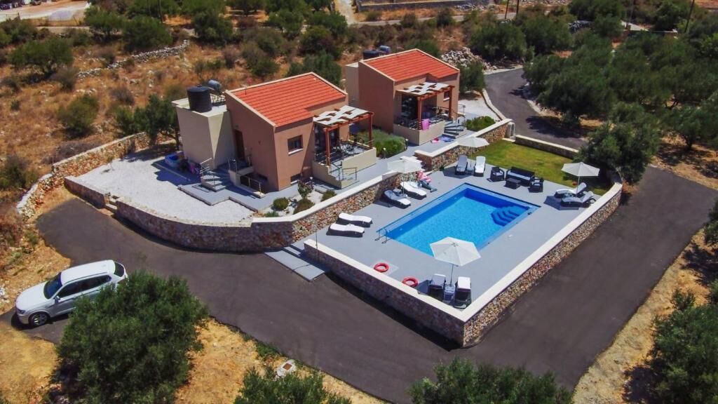 Vue aérienne d’un complexe hôtelier avec une piscine, des chaises longues et une voiture blanche garée à proximité.