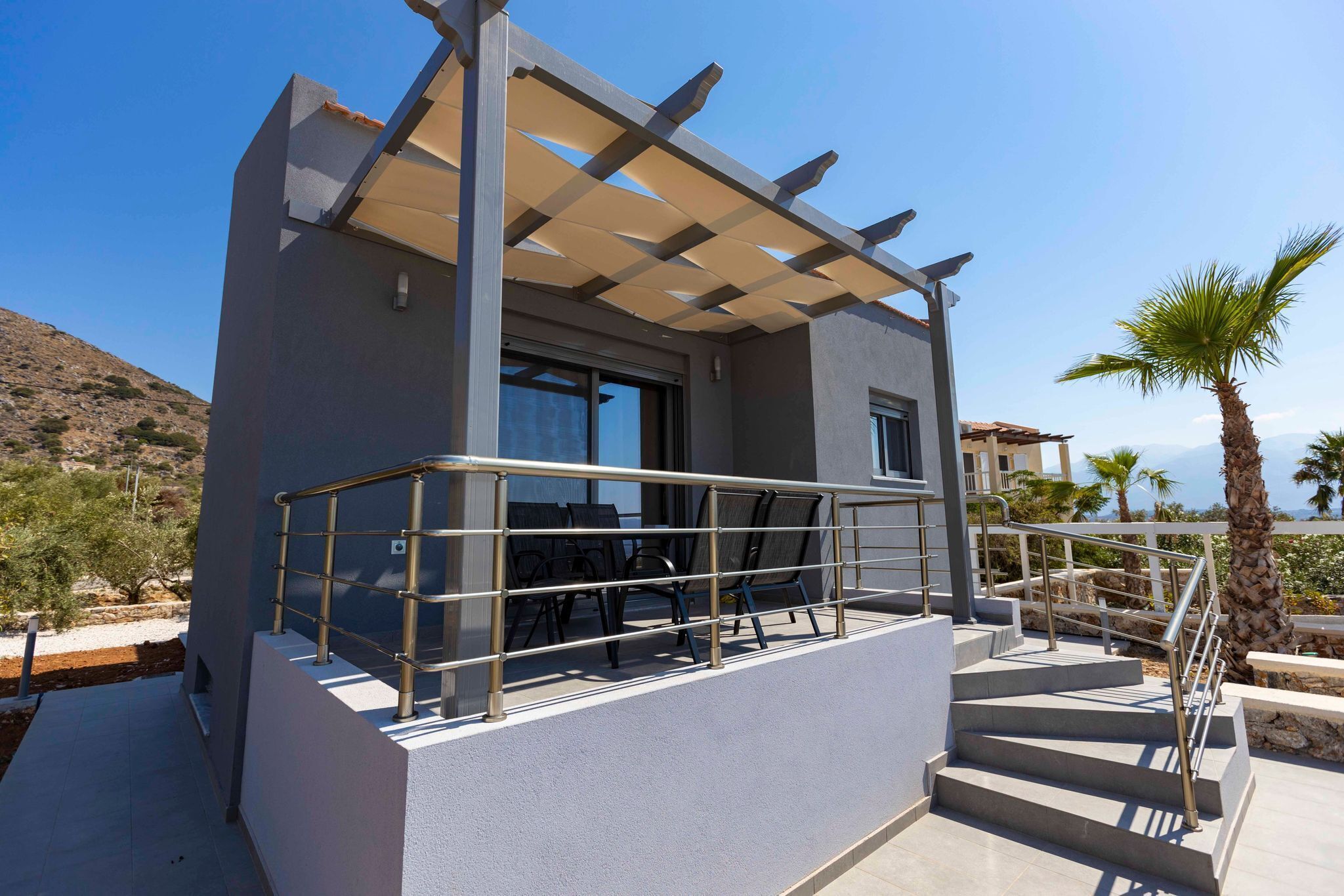 A modern outdoor balcony with a pergola, a staircase, and outdoor seating.