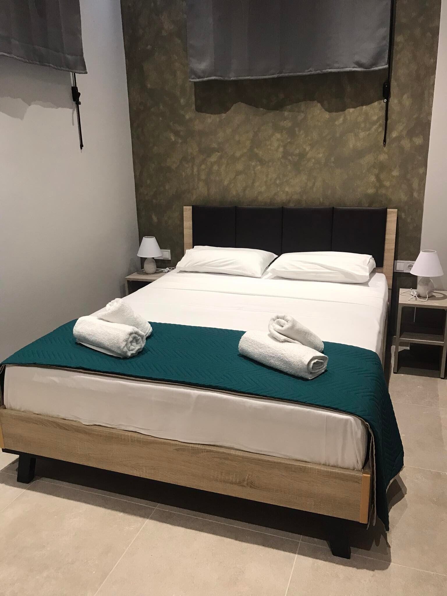 A neatly made bed with white linens and teal bedding, two bedside tables with lamps, and a dark headboard.
