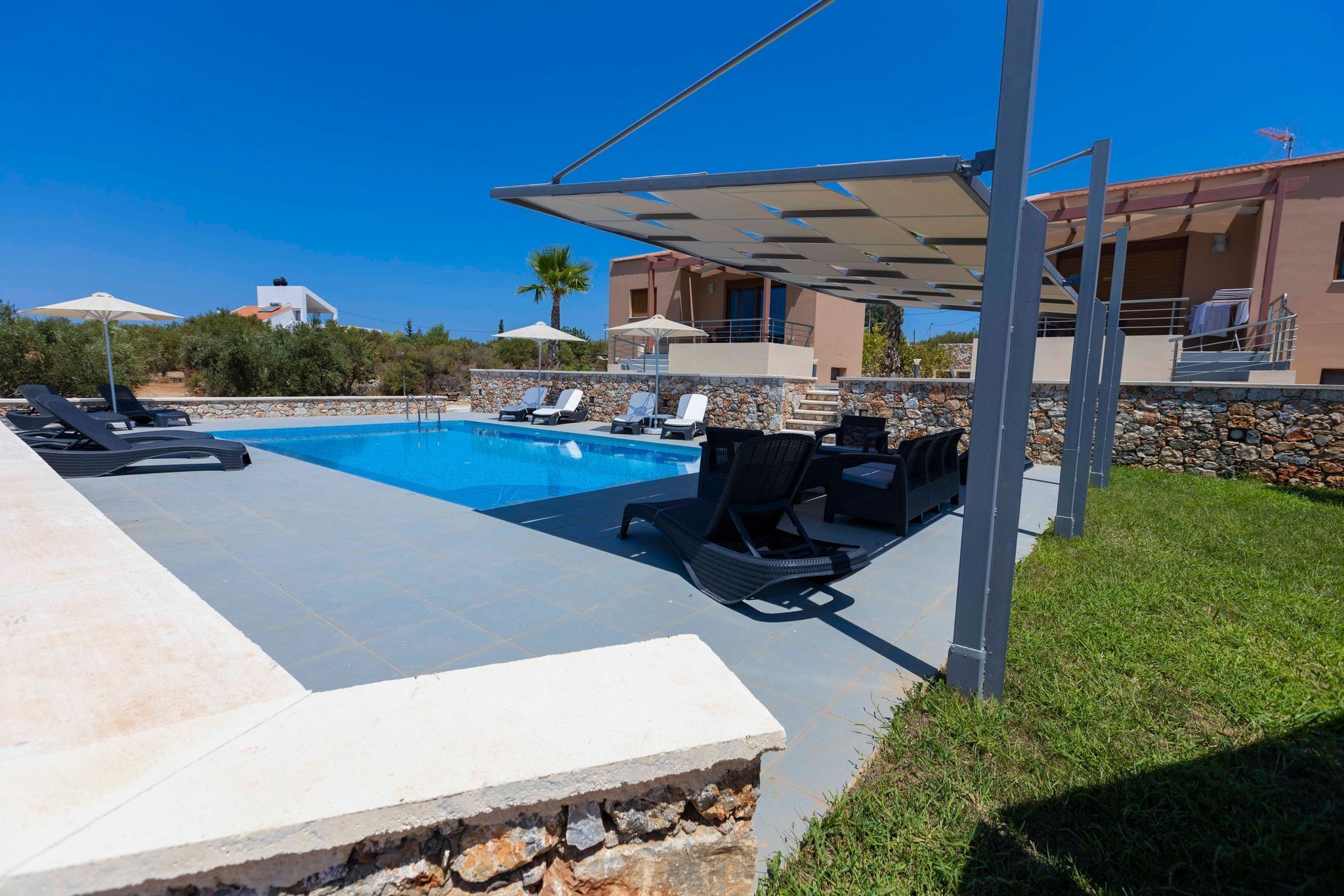 A pool area with lounge chairs, a pergola, and a stone wall.