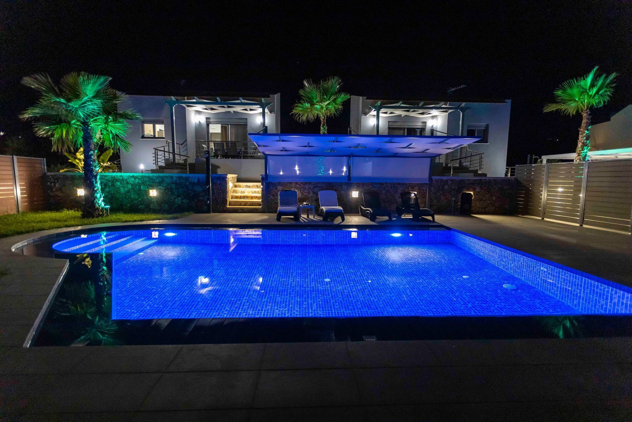 A modern house with a swimming pool, outdoor seating, and a well-lit entrance.