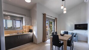 Een moderne keuken met donkere kastjes, een houten aanrechtblad en een inbouwoven. Er is een eethoek met een tafel en stoelen, een tv aan de muur bevestigd, en een schuifdeur naar een balkon.
