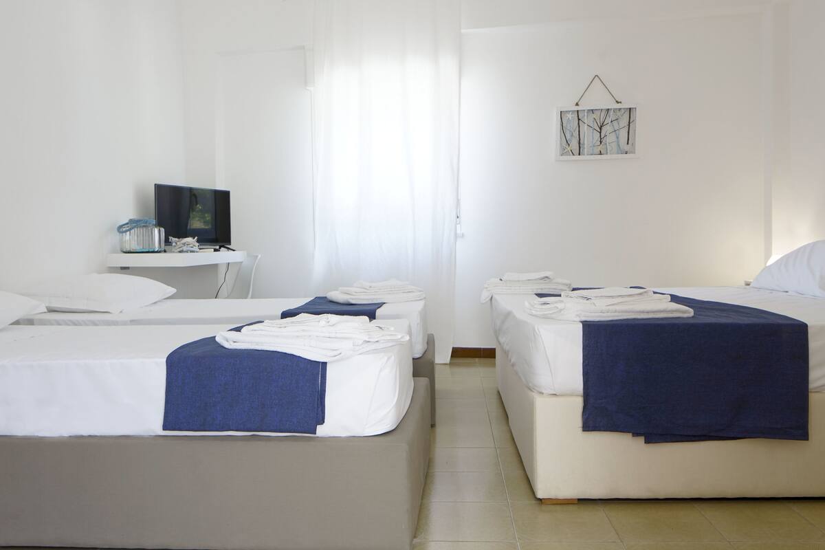 A hotel room with two beds, a small desk with a television, and a window with curtains.