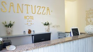 Un hall d’hôtel avec une enseigne murale indiquant « HÔTEL SANTUZZA » et un comptoir d’accueil.