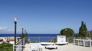 Une terrasse en bord de mer, avec des bancs blancs et une balustrade, d’où l’on a une vue sur l’océan.