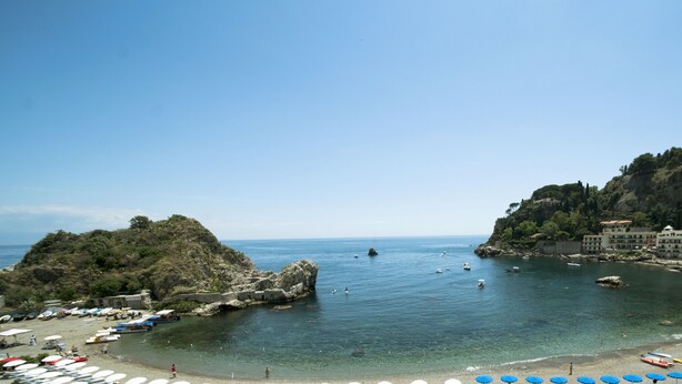 Une plage côtière aux eaux cristallines, où l’on peut voir des bateaux et des parasols.