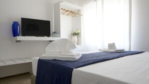 Une chambre d’hôtel avec un lit, une télévision, une étagère avec un vase et une fenêtre avec des rideaux.