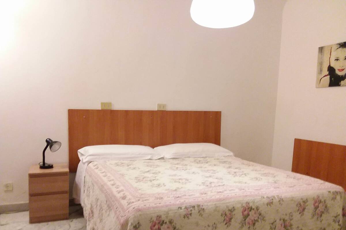 A bedroom with a wooden headboard, a bedside table with a lamp, and a floral bedspread.