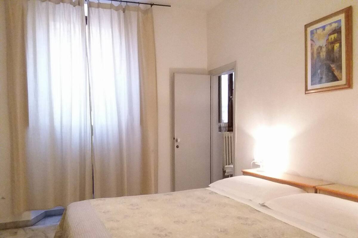 A hotel room with a bed, a door, a radiator, and a painting on the wall.
