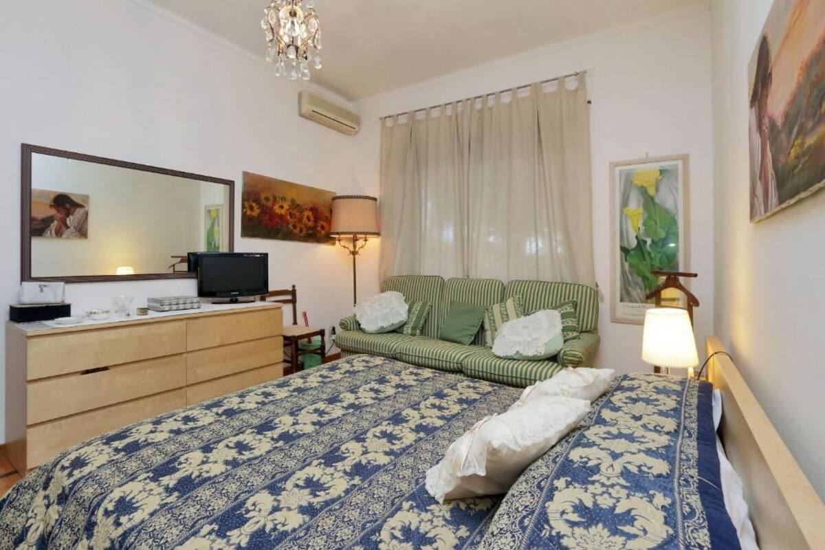 A bedroom with a bed, a dresser, a television, a lamp, and a painting.