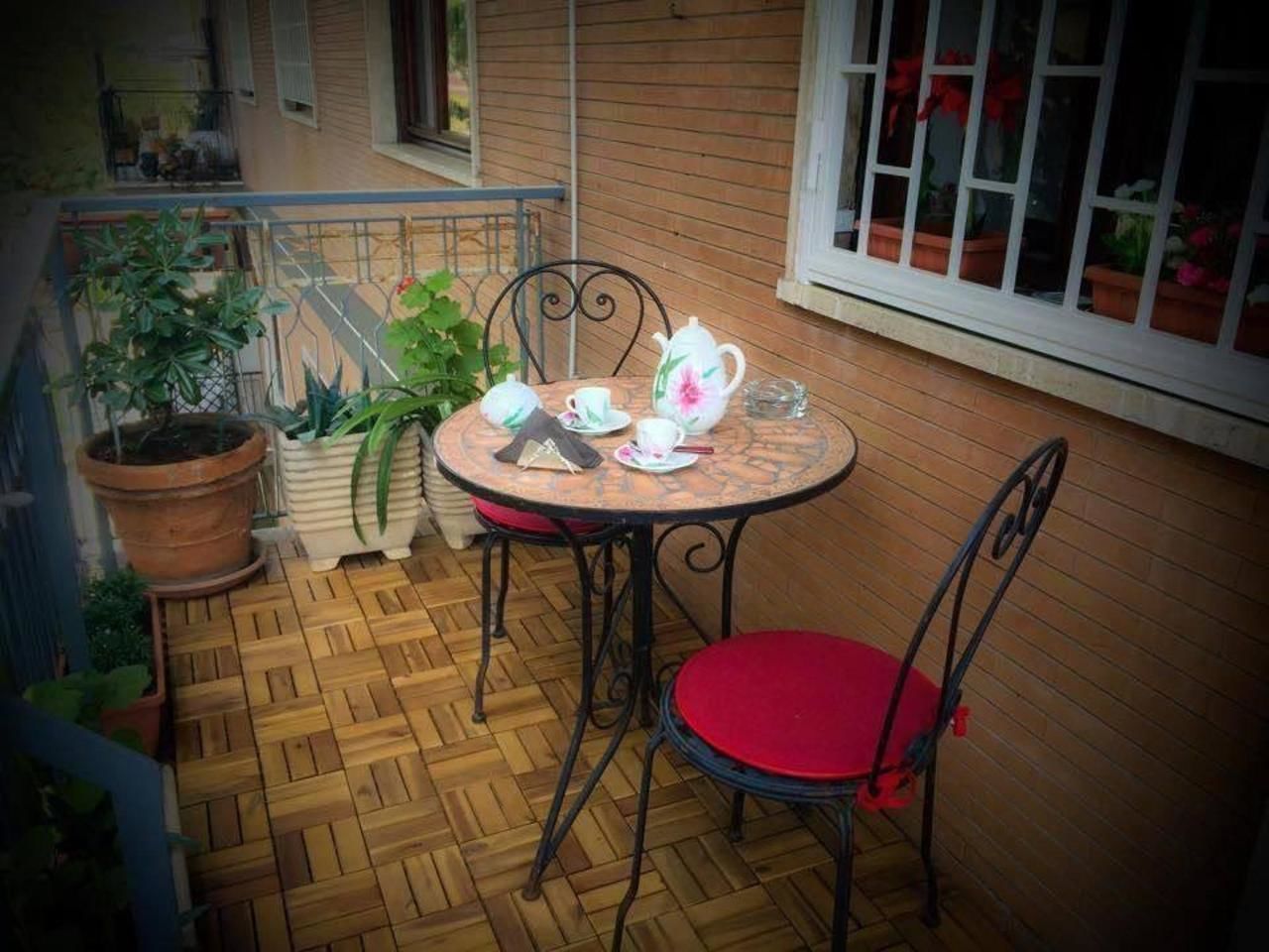 Eine kleine Terrasse mit einem runden Tisch, zwei Stühlen, einem Blumentopf und einem Fenster mit Pflanzen.