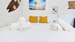Ein ordentlich bezogenes Bett mit weißen und senffarbenen Kissen, ein tropisch gestaltetes Bild und eine dekorative Wandarbeit.