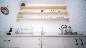 A kitchen with white cabinets, a kettle, a coffee maker, and a shelf with kitchenware. - Dayos Unique Suites (Eilat)