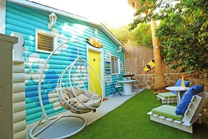 Uma cabana colorida com uma cadeira de balanço, uma mesa pequena e área de estar ao ar livre.