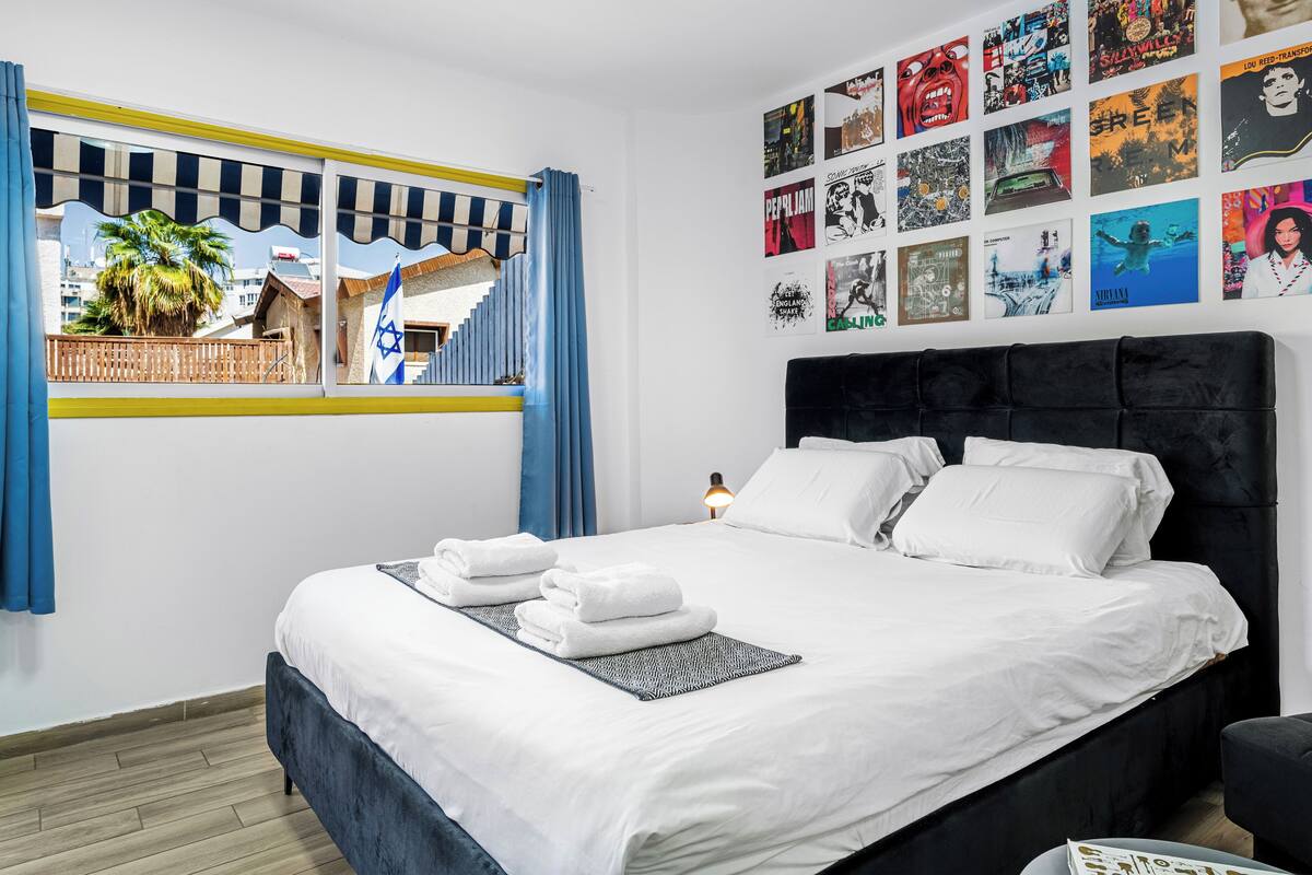 A hotel room with a bed, a window with curtains, and a wall decorated with various posters.
