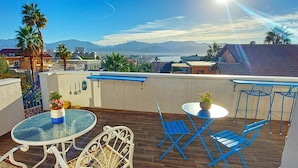 Eine Dachterrasse mit einem Glastisch, blauen Stühlen und einem Topfpflanzen.