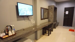 A modern hotel reception area with a flat-screen TV mounted on the wall, a coffee machine, a bottle of water, and a tray with snacks. - Ploenjai Hotel Ranong (Ranong)